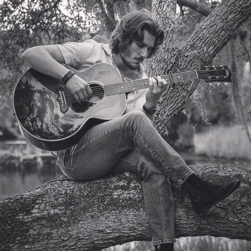 George Pennington playing acoustic guitar in a tree
